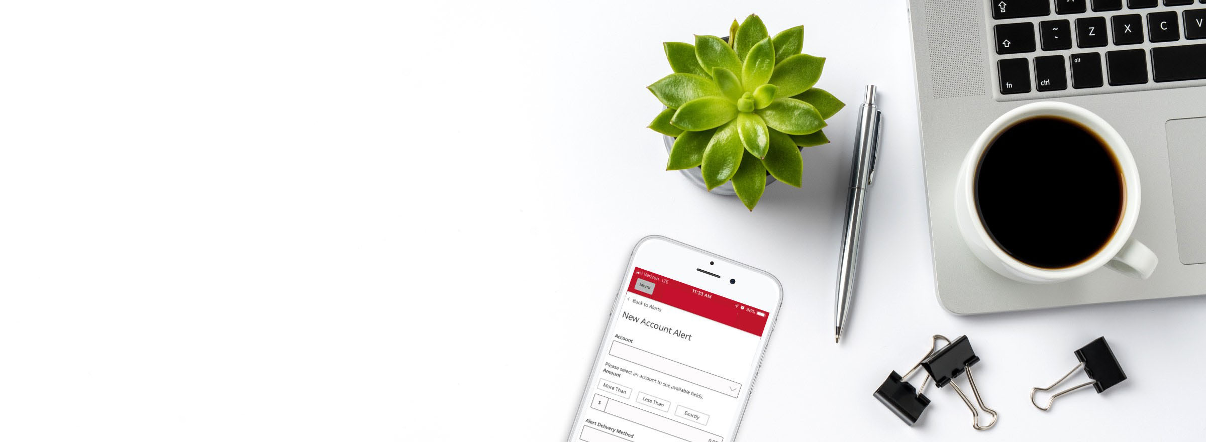 Phone with Ariston Credit Union app alerts screen, laptop on tabletop